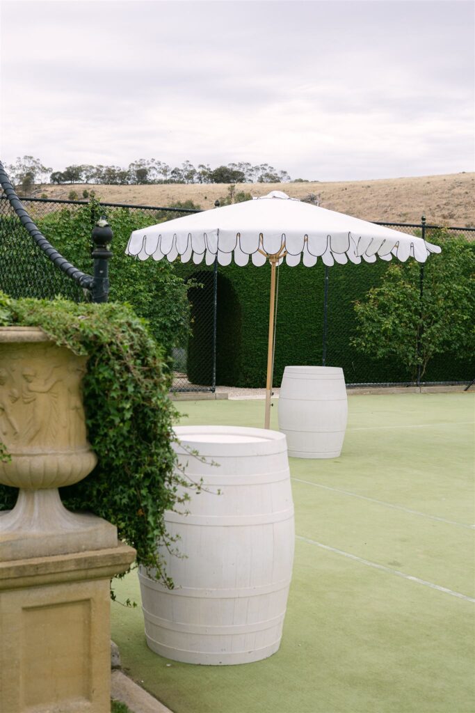 Manicured garden at Mandalay House and Garden in the Adelaide Hills, South Australia, styled with a white striped umbrella and wine barrel details. One of South Australia's most sought after wedding venues.