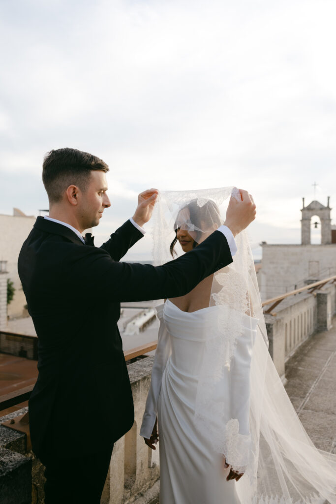 Groom lifting the bride’s veil during an intimate destination wedding at Masseria Amastuola in Puglia, Italy, captured in a refined editorial style.
