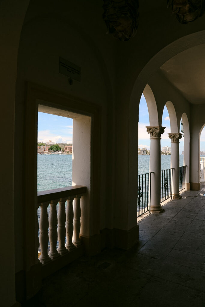 View through a heritage archway at Manly Pavilion framing Sydney Harbour beyond