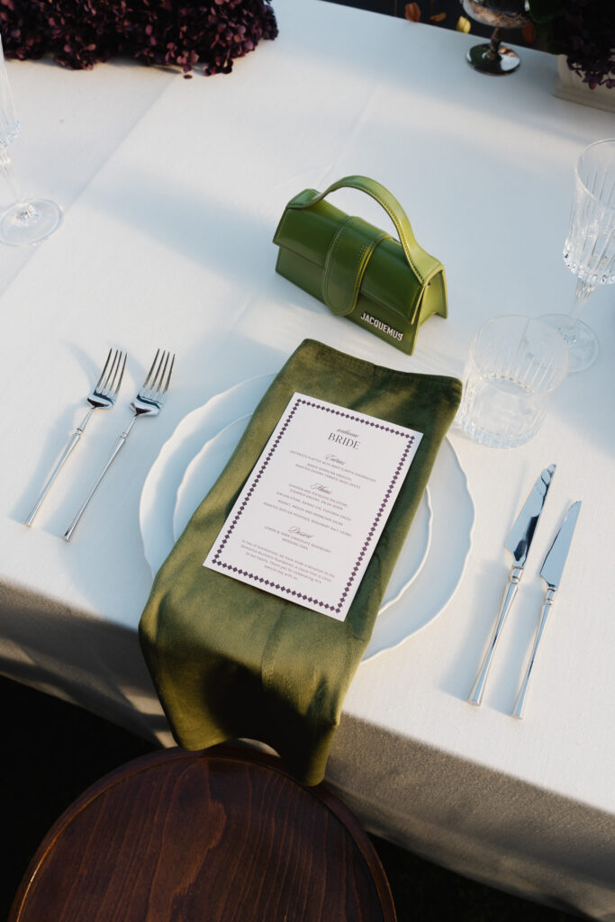 Wedding table setting with green Jacquemus bag, stationery and white linen.