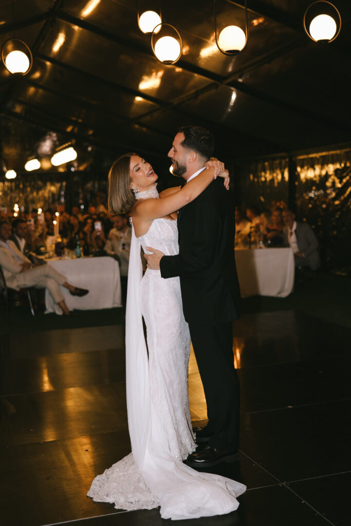 Bride and groom sharing their first dance inside a darkened marquee with warm pendant lighting.