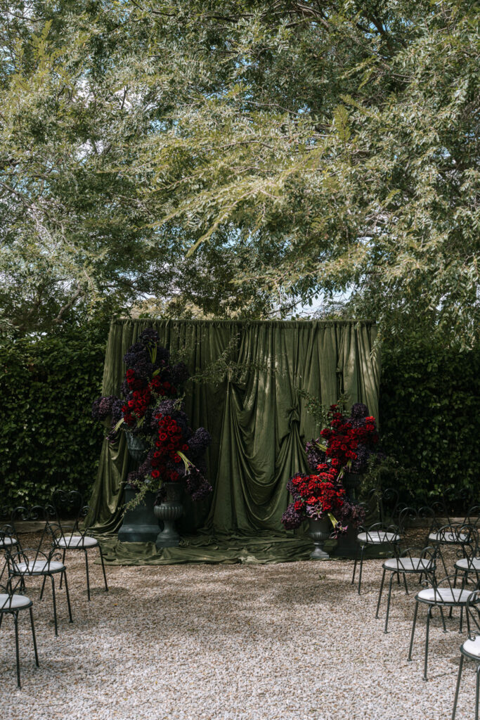 Outdoor wedding ceremony at Whites Valley Estate with dark green draping and red and plum floral arrangements.
