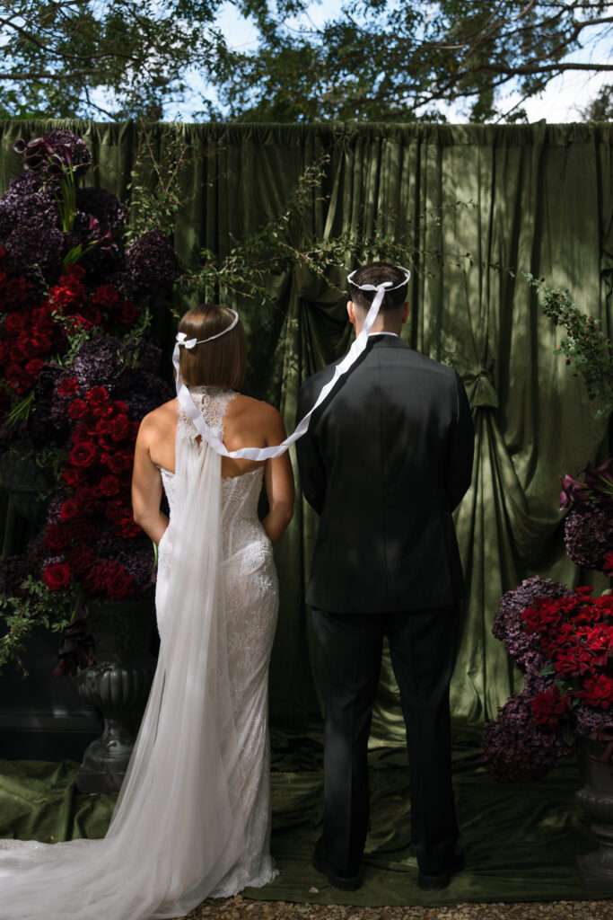 Bride and groom wearing Stefana crowns during an outdoor Greek Orthodox wedding ceremony.