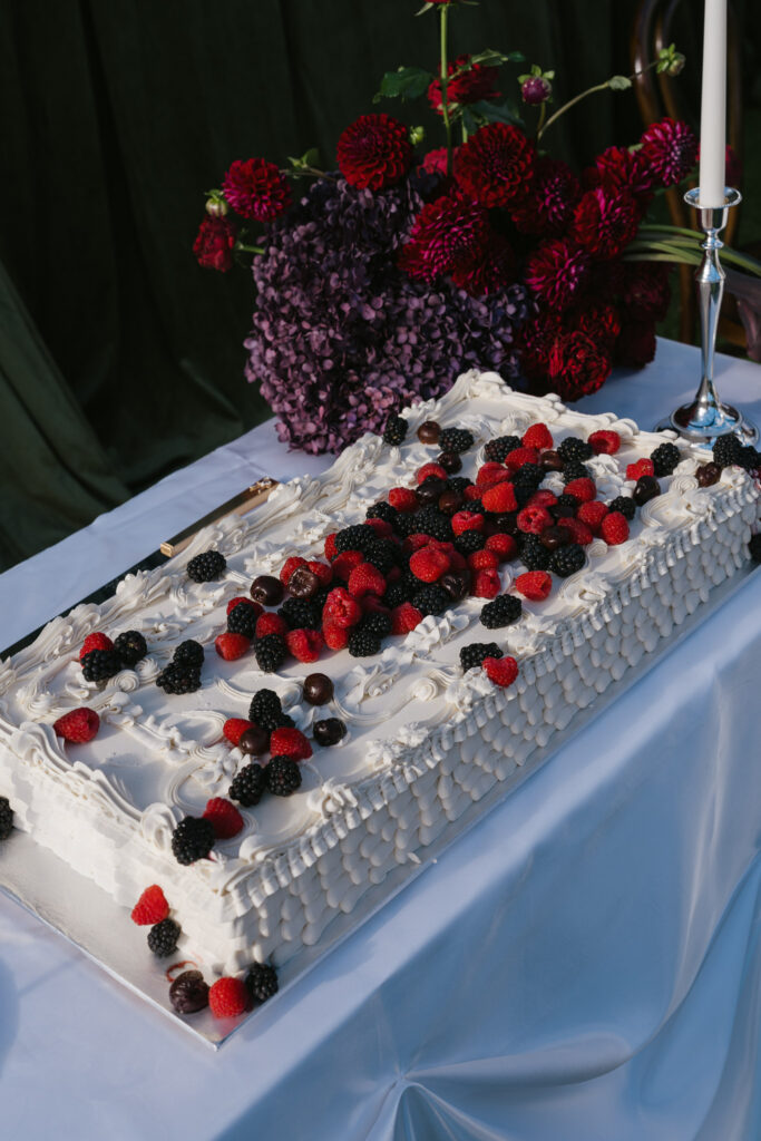 White wedding cake decorated with fresh raspberries and blackberries with red and plum dahlia florals