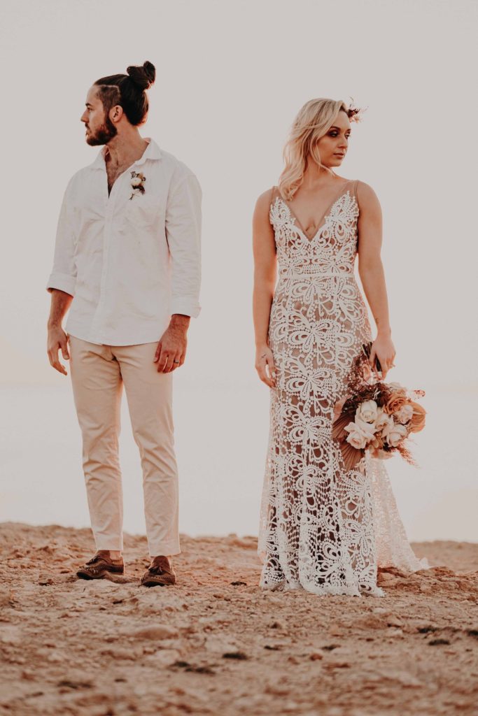 an eloping couple stand on a clifftop, faces turned away from each other, connection