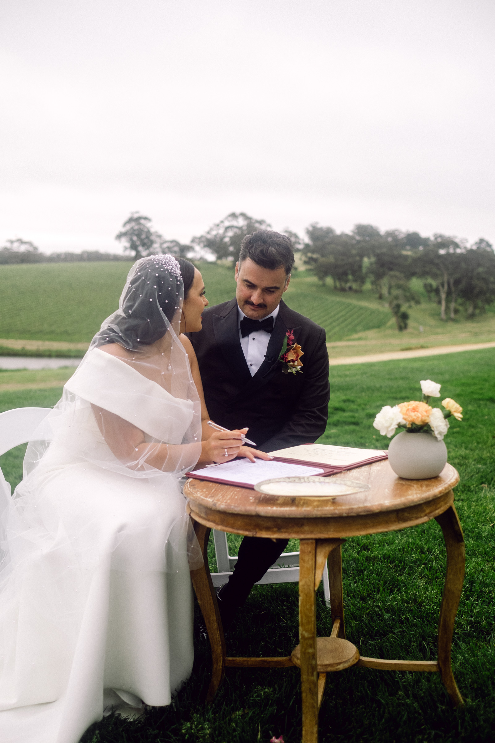 a bride and groom sign their paperwork with rolling hills in the background at Longview Vineyard in the Adelaide Hills