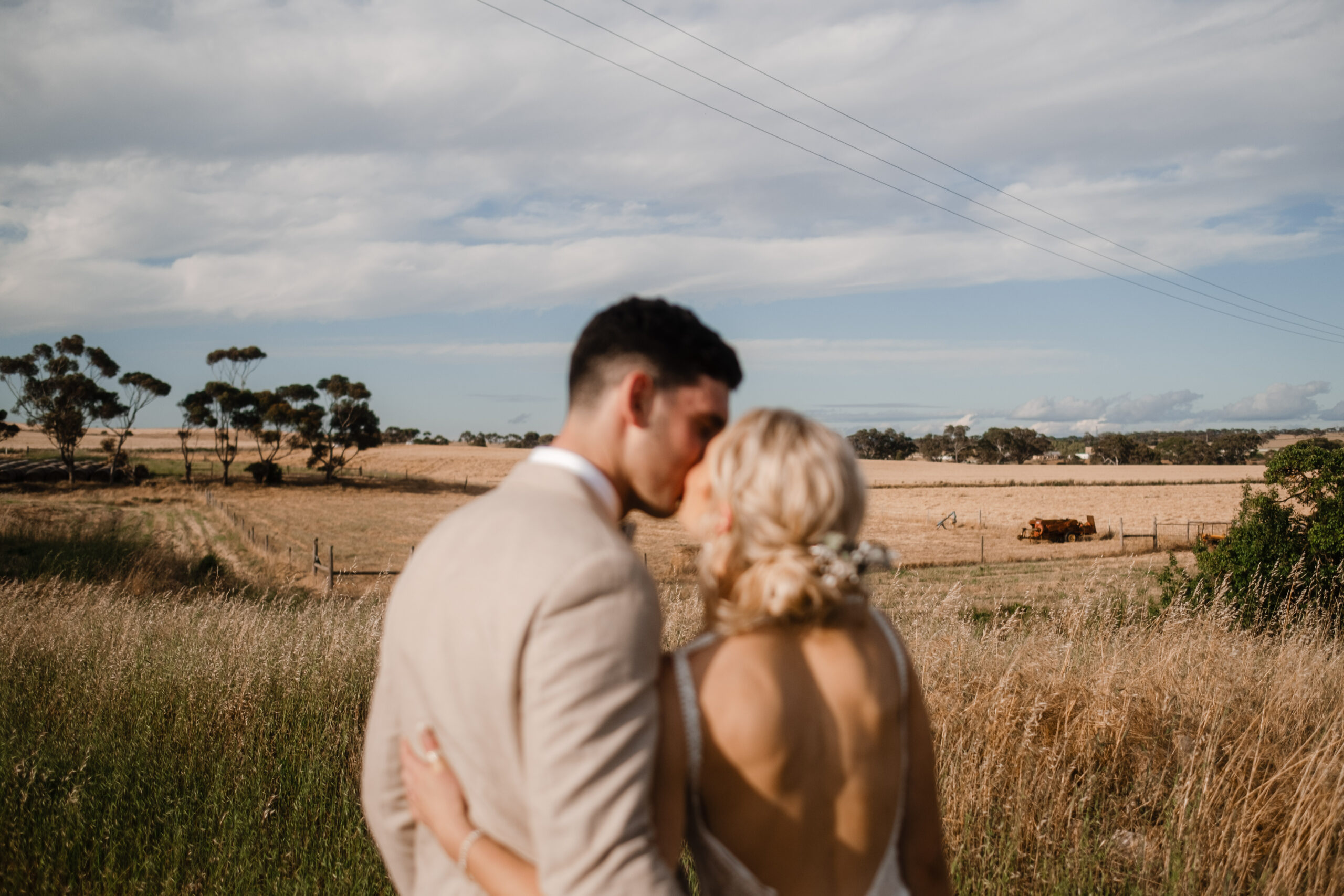 a bride and groom are blurred in the foreground, kissing, with the beige fields of Strathalbyn in the background in focus