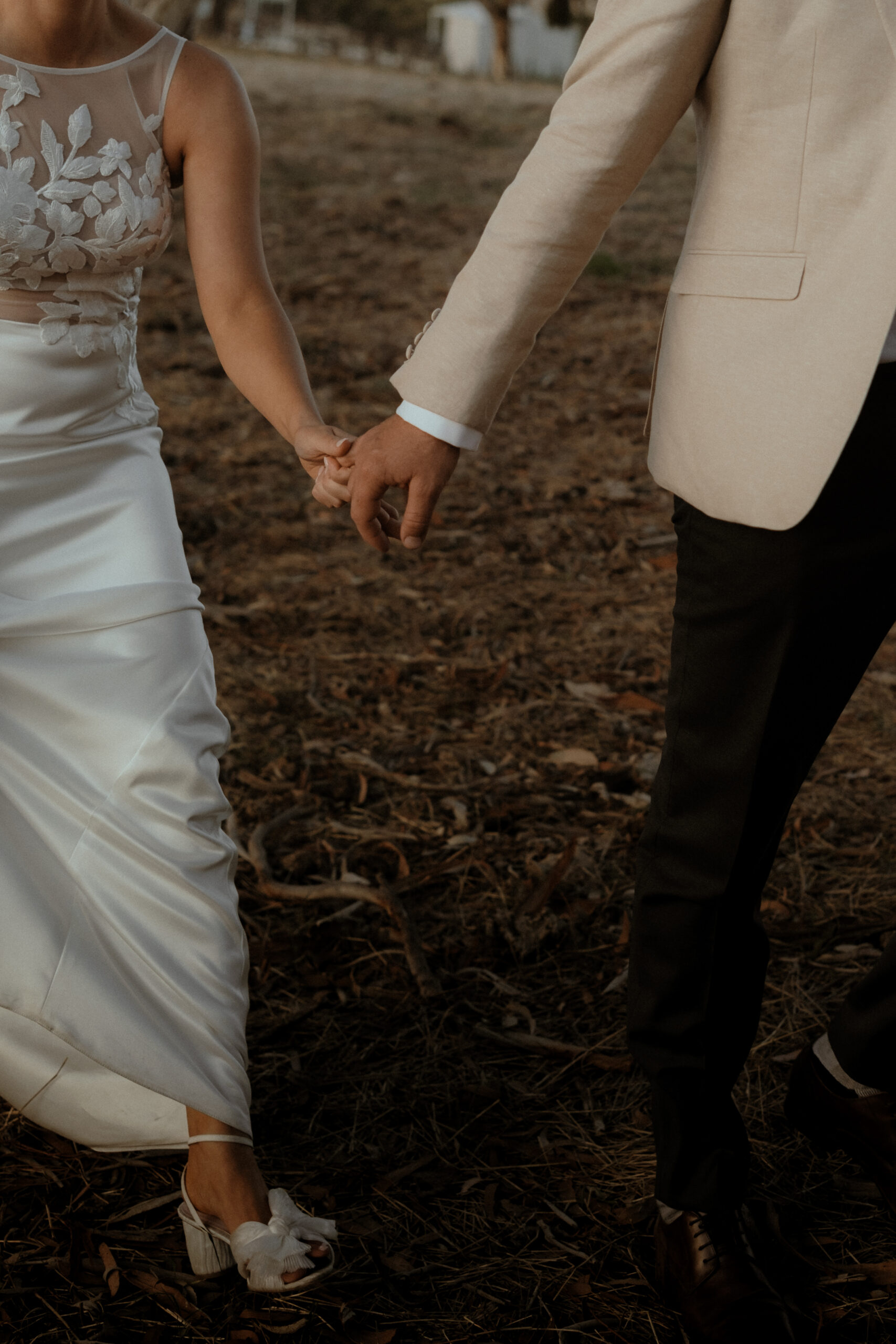 a groom holds his brides hand and leads her through a field toward their destination
