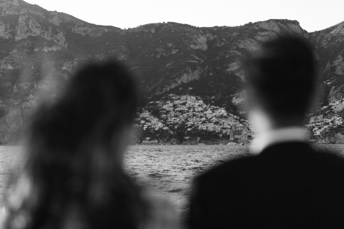 a black and white photograph of a bride and groom blurred out in the foreground, looking at the Positano coastline in the distance during their destination wedding.