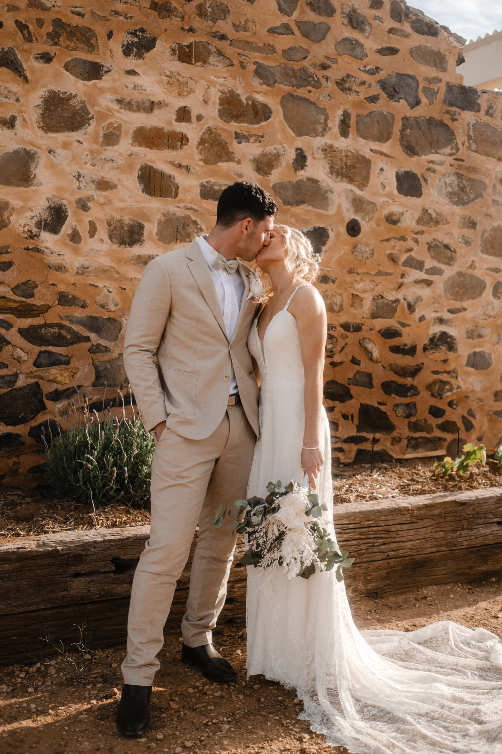 a bride and groom share a kiss in front of old stone building at Bremer Farm in Strathalbyn