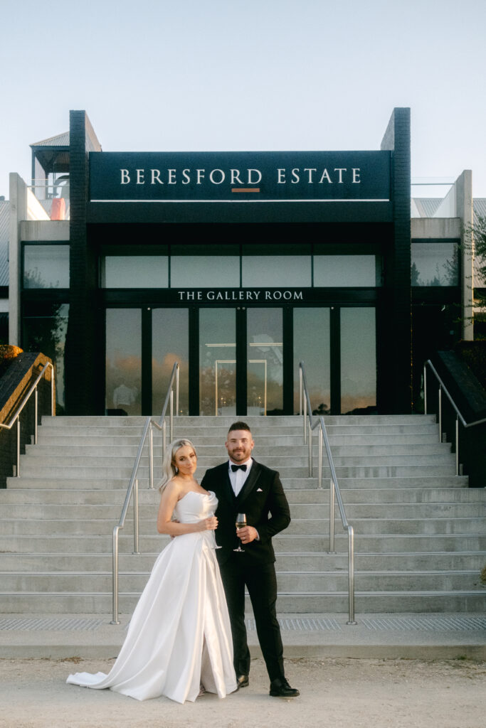 a bride and groom stand in front of Beresford Estate, a luxurious modern tasting pavilion
