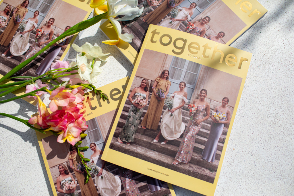 four copies of Together Journal magazine and wedding blog lay spread out on a white stone surface with some flowers as décor 