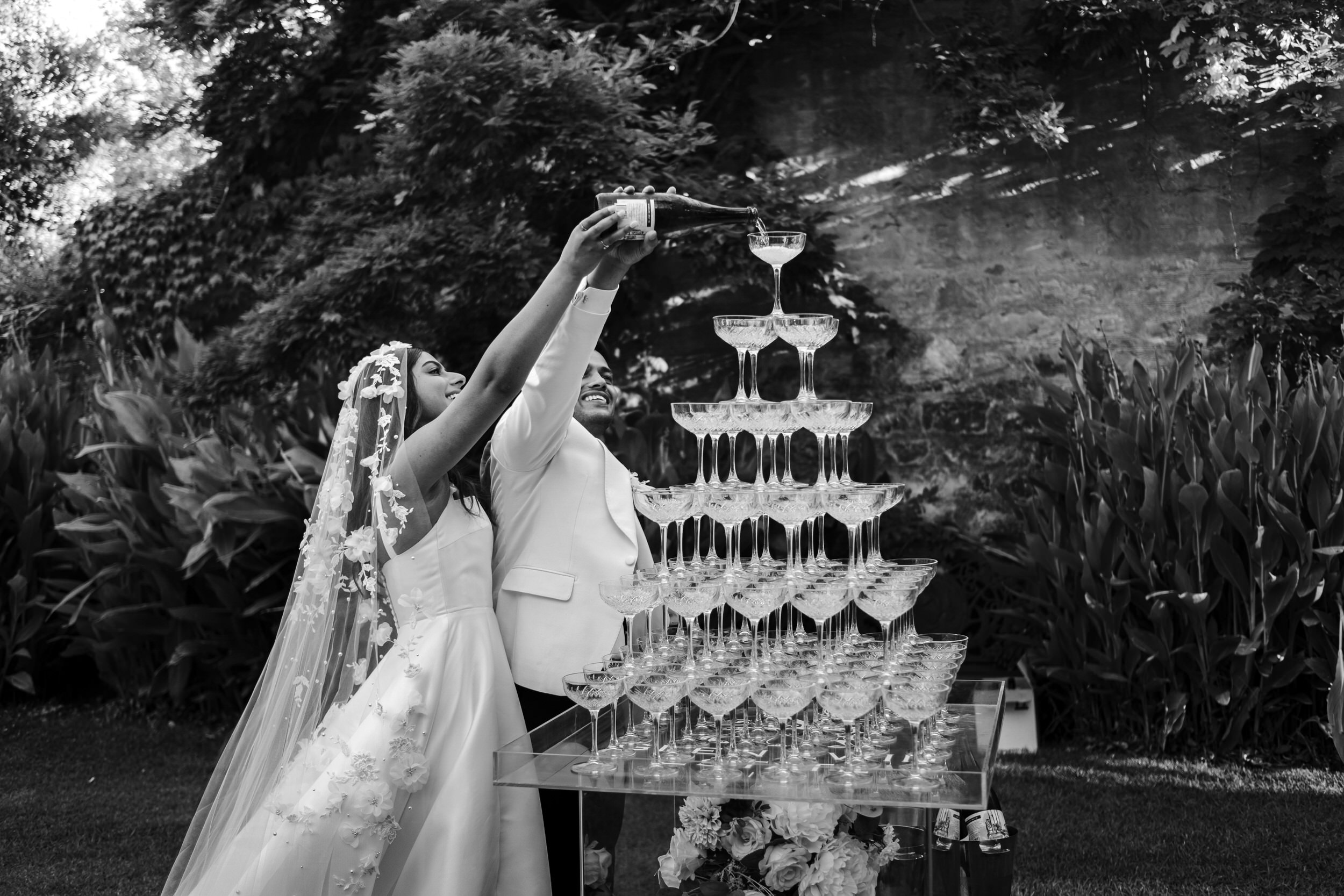 a bride and groom hold a champagne bottle and pour into their champagne tower at glen ewin estate