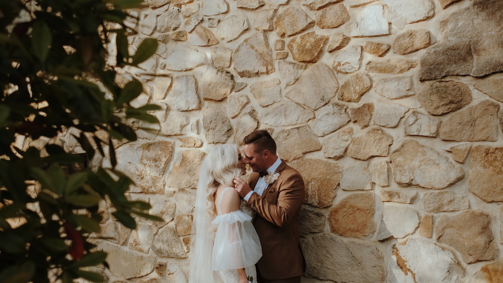 a bride and groom share an embrace in front of a stone wall, a screengrab from their wedding videographer