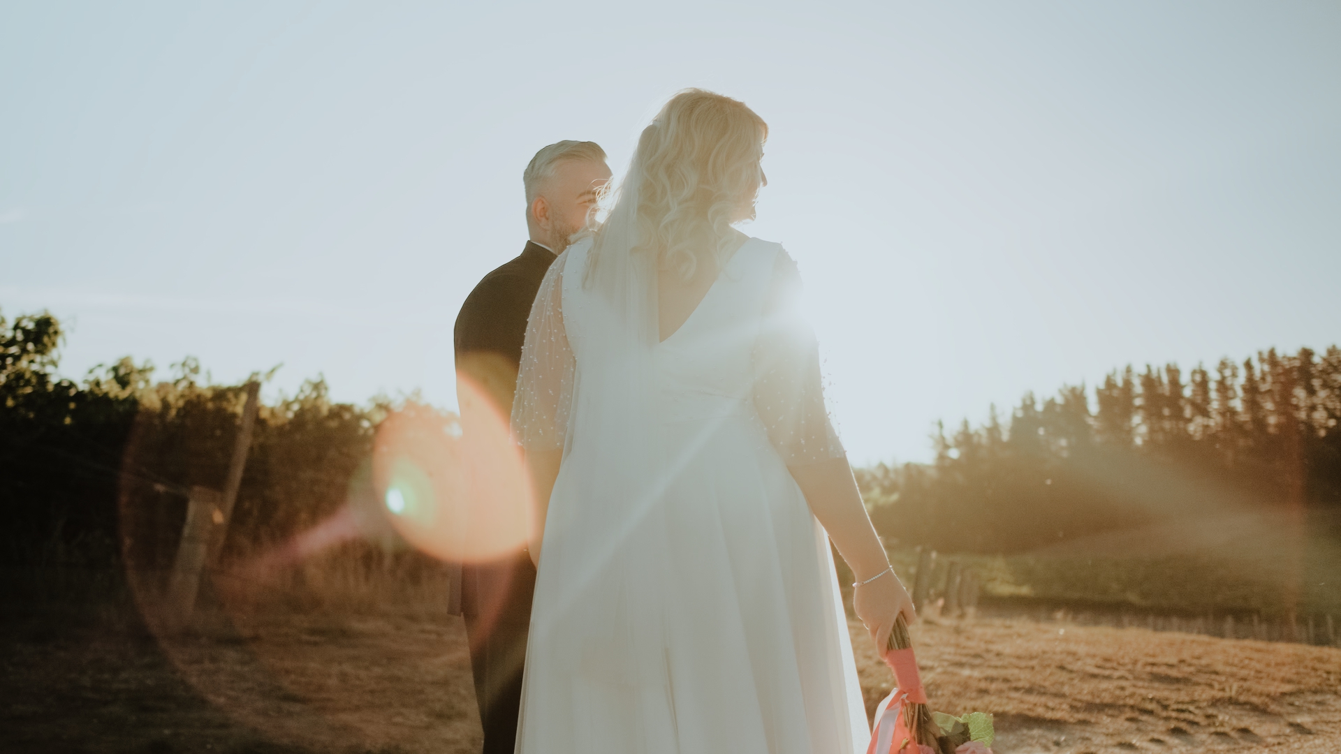 a bride and groom walk down a driveway at sunset at The Lane Vineyard