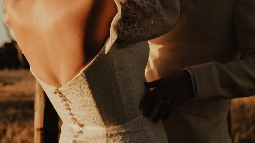 a close up of a groom touching his wife's waist as she flings her arms around his neck during golden hour at Woodburn Homestead