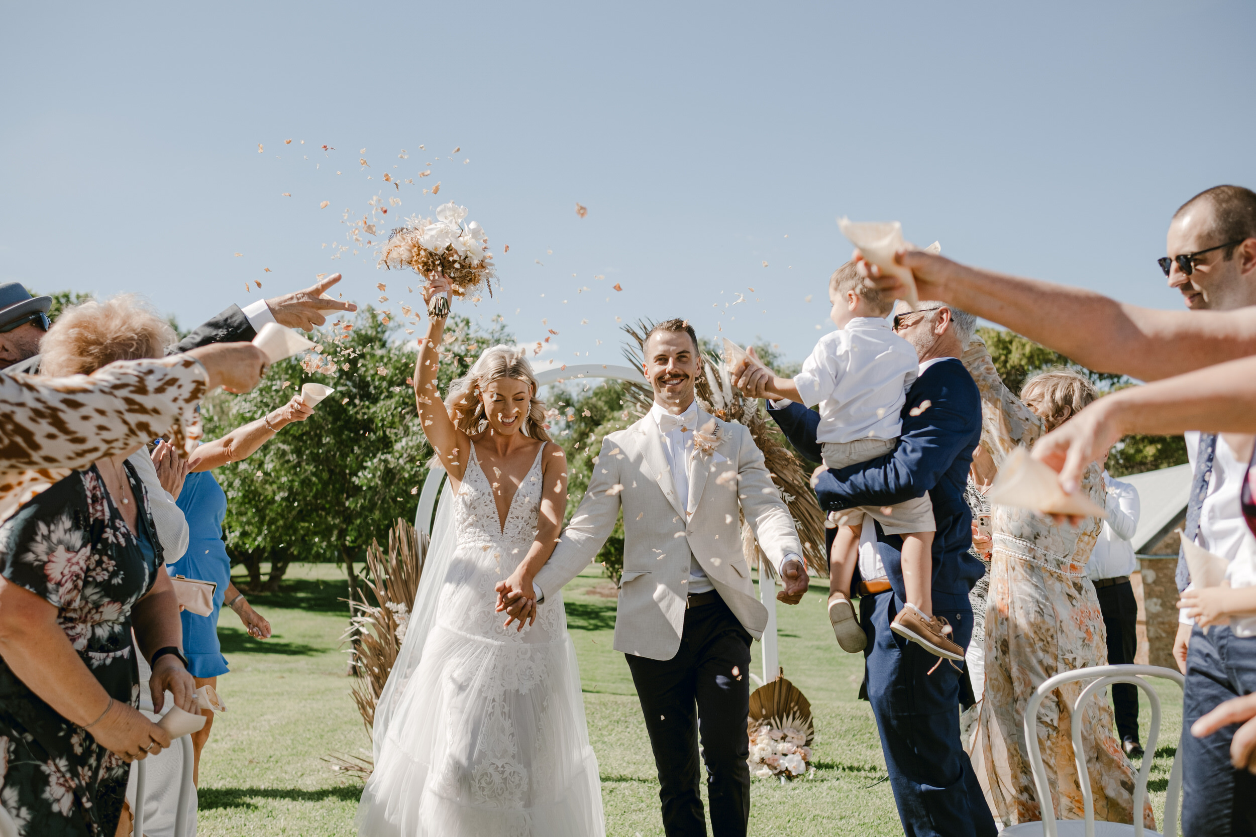 a bride and groom are showered in rose petals as they walk down the isle hand-in-hand at Paxton Wines