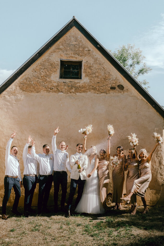a bridal party spray champagne at an old stone building at Paxton Wines