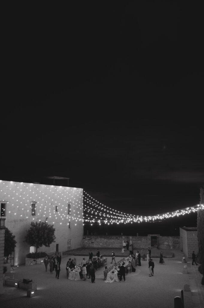 Black and white view of the evening reception under festoon lights at Masseria Amastuola