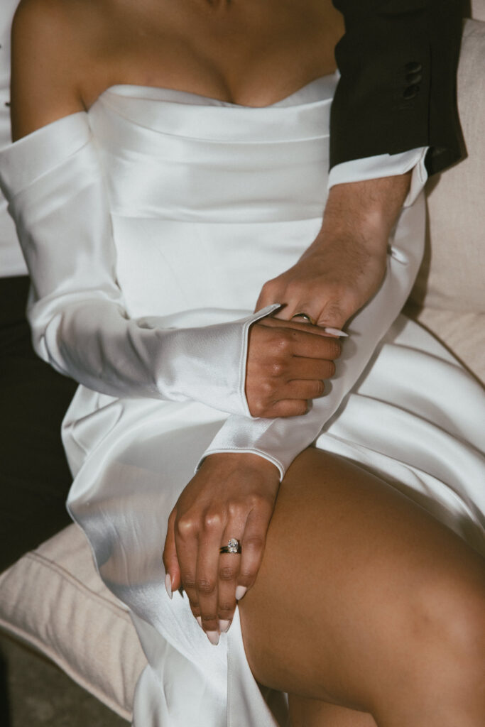 Intimate close-up of the bride seated in her wedding dress holding the groom's hand during the evening celebration