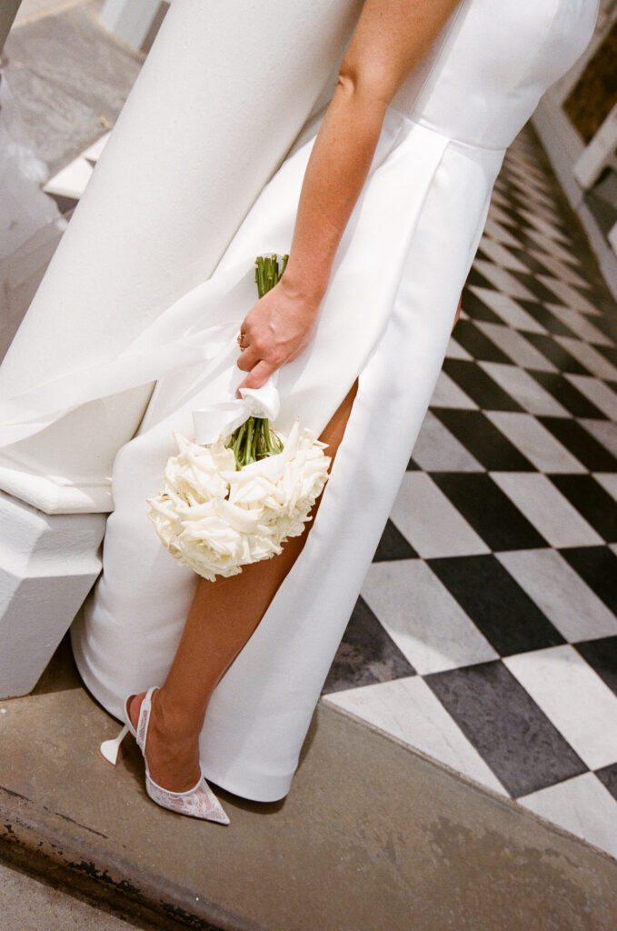 35mm film wedding photography, close up of bride's white heels and bouquet on black and white checkered marble floor
