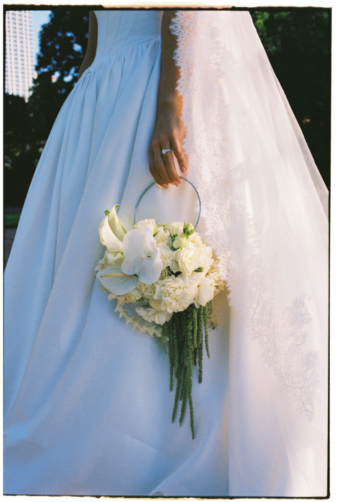 35mm film wedding photography, close up of bride holding a cascading white bouquet with trailing greenery against a full skirt gown
