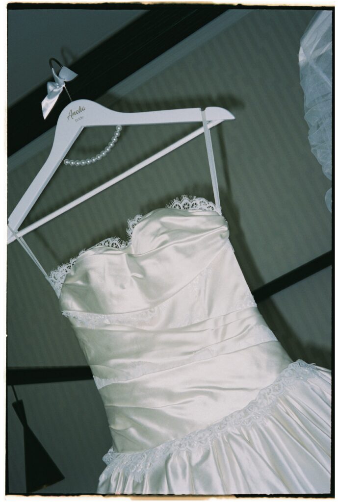 35mm film wedding photography, wedding dress on hanger with pearl necklace and lace detail, Evelina Katarzyński
