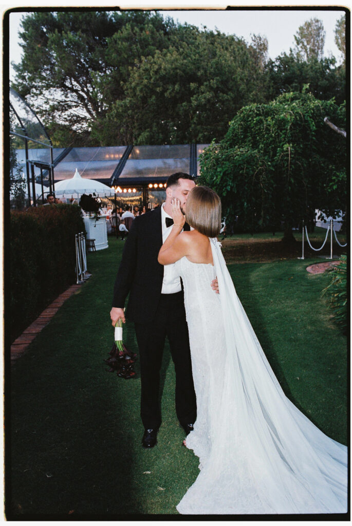 35mm film wedding photography, bride and groom walking at dusk with long cathedral veil, garden venue, Evelina Katarzyński
