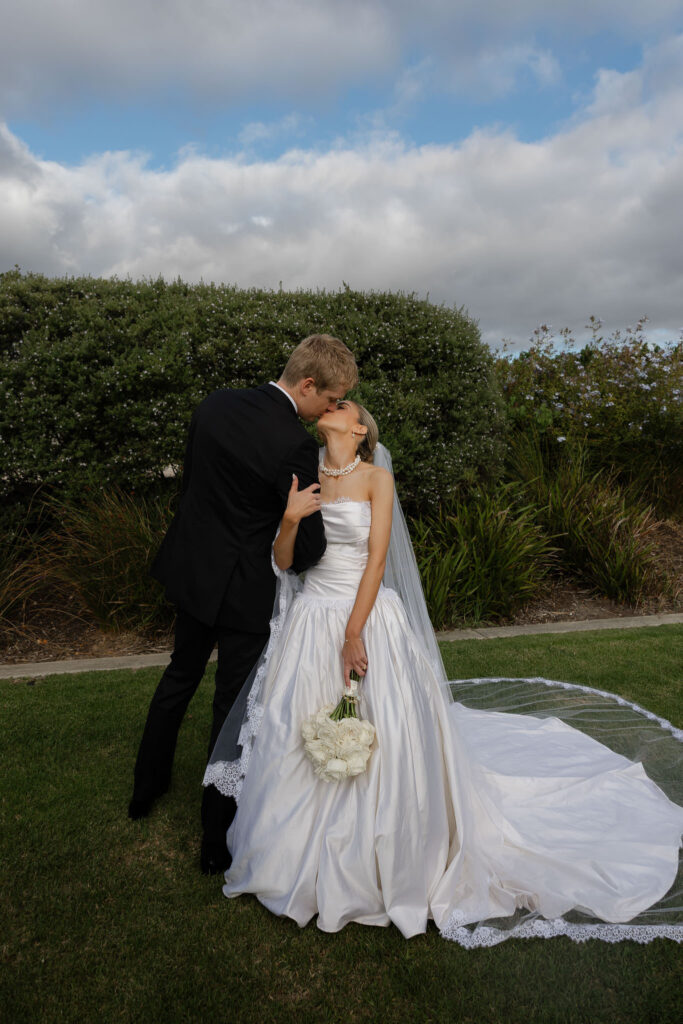 Bride and groom sharing a kiss on the Pepper Tree Lawns at Beresford Estate, hedging enclosing the space behind them.